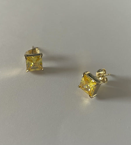 Pair of yellow gemstone stud earrings on a light gray background