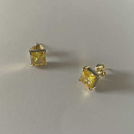 Pair of yellow gemstone stud earrings on a light gray background