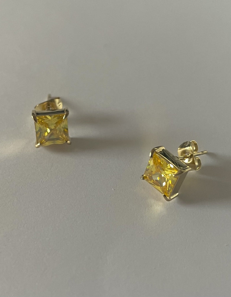 Pair of yellow gemstone stud earrings on a light gray background